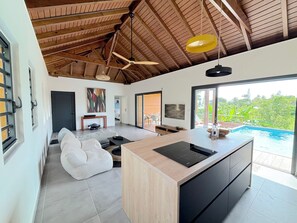 A spacious living area with a large island, a ceiling fan, and a view of a swimming pool. - LA PETITE VILLA 2CH PISCINE PROCHE MER (Sainte-Anne)