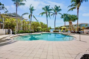 A swimming pool with palm trees, a building with a flat roof, and a clear sky.