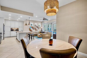 A modern kitchen with white cabinets, a dining area with a marble table, and a living space with a sofa and decorative wall art.