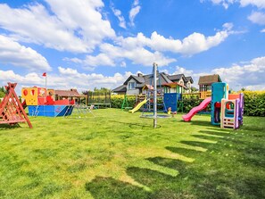 A playground with various play structures, a flagpole, and a house in the background.