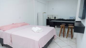 A hotel room with a bed, a desk, a kitchen area, and a TV mounted on the wall.