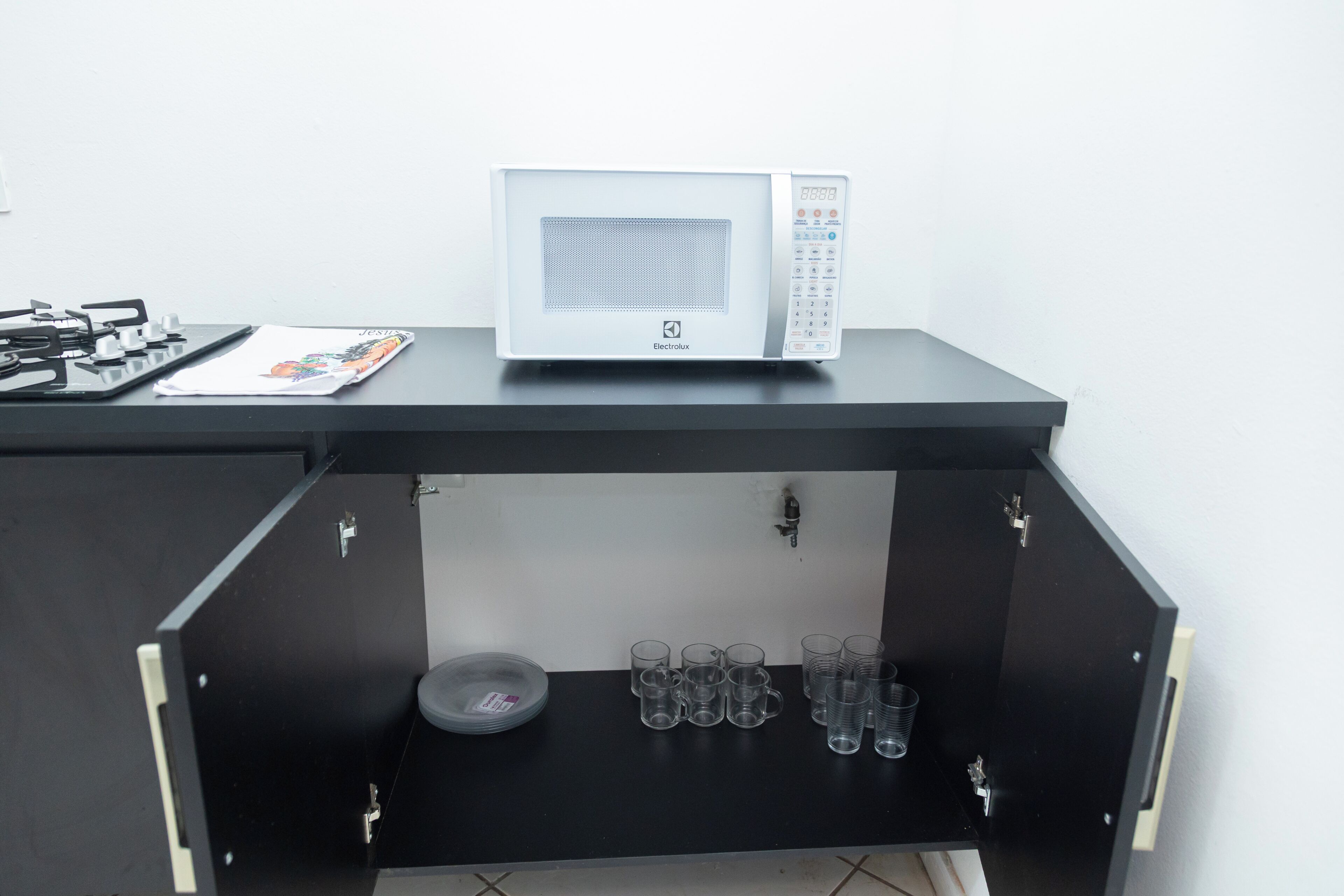 A microwave on a black countertop, a gas stove, and a drawer with multiple glasses.