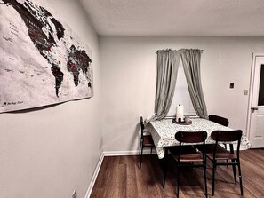 Un coin repas avec une table et des chaises, une carte du monde accrochée au mur et une fenêtre avec des rideaux.