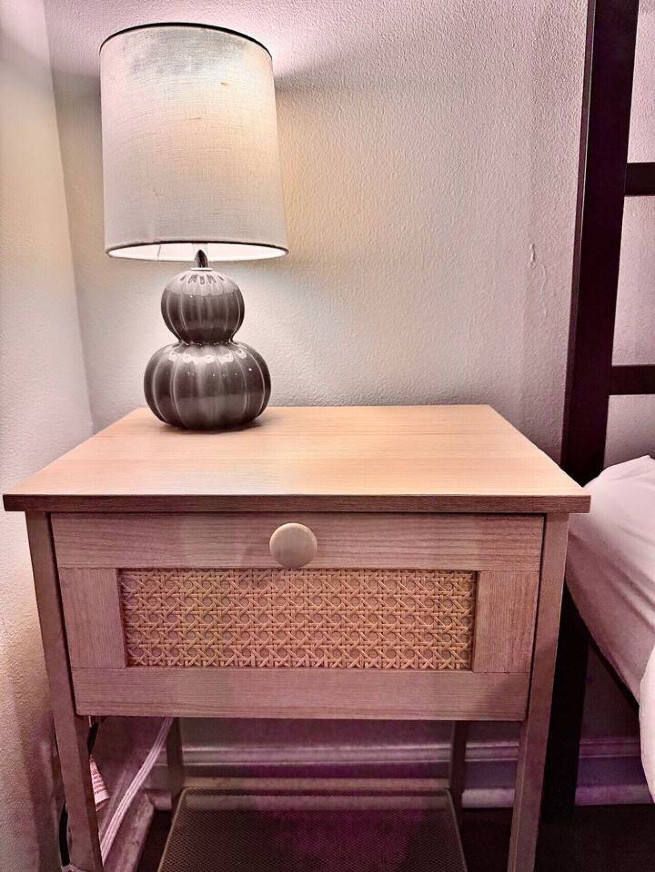 Une table de chevet en bois, dotée d’une lampe, d’un tiroir et d’un panneau texturé.