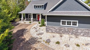 A two-story house with a stone foundation, a red door, and a grey roof. - Fish Creek home- near downtown w/ Fire pit (Fish Creek)