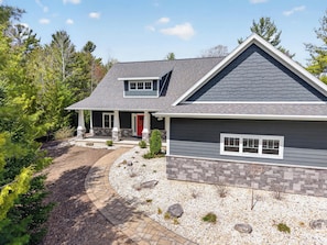 A two-story house with a stone foundation, a red door, and a grey roof.