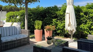 Eine Terrassengruppe im Freien mit Korbmöbeln, einem weißen Sonnenschirm und Blumentöpfen.