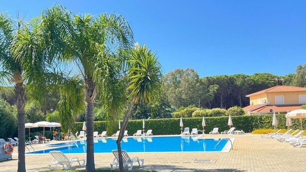 Ein Schwimmbad mit Liegestühlen, Palmen und einem Gebäude im Hintergrund.
