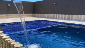 Una piscina con borde de tronco de madera y fuente de agua.