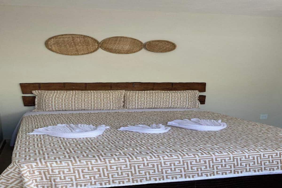 Ein Bett mit gemustertem Bettbezug, einem hölzernen Kopfteil und drei gewebten Wandgestaltungen.