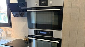 A modern kitchen with a built-in oven and microwave, wooden cabinets, and a stainless steel backsplash.