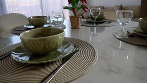 A dining table set with bowls, plates, and cutlery, a woven placemat, and a potted plant.