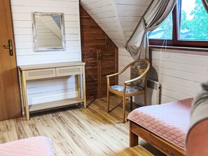 A bedroom with a wooden floor, a bed, a chair, a small table, and a window with curtains. - Willa Kinga z kominkiem by Interhome (Rewal)