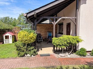 A wooden building with a covered porch, a small shed, and neatly trimmed bushes. - Willa Kinga z kominkiem by Interhome (Rewal)