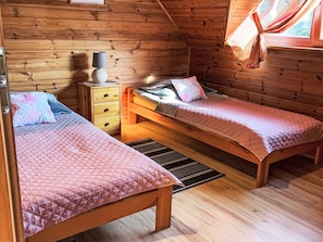 Ein gemütliches Blockhauskabinenzimmer mit zwei hölzernen Betten, einem Nachttisch und einem Fenster mit Vorhängen.