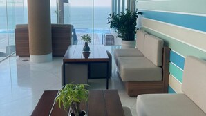A modern lounge with a view of the ocean, featuring a wooden table, a sofa, and a potted plant. - A la Carte - Coralie Luxury Seaview Aprtment (Đà Nẵng)