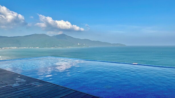 A clear blue sky, a swimming pool, and a distant view of a coastline with mountains. - A la Carte - Coralie Luxury Seaview Aprtment (Đà Nẵng)