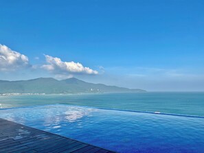 A clear blue sky, a swimming pool, and a distant view of a coastline with mountains. - A la Carte - Coralie Luxury Seaview Aprtment (Đà Nẵng)