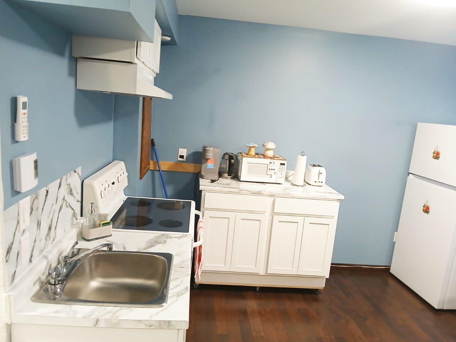 A compact kitchen with a sink, stove, microwave, and white cabinets.