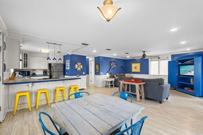 Eine moderne Küche mit Kochinsel, Barhocker, Esstisch und Wohnbereich inklusive Sofa und Fernseher.