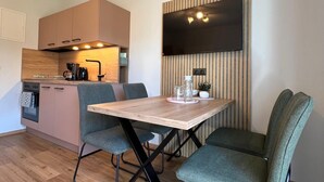 Une cuisine compacte dotée d’appareils électroménagers modernes, une table à manger avec des chaises et un téléviseur à écran plat fixé au mur.