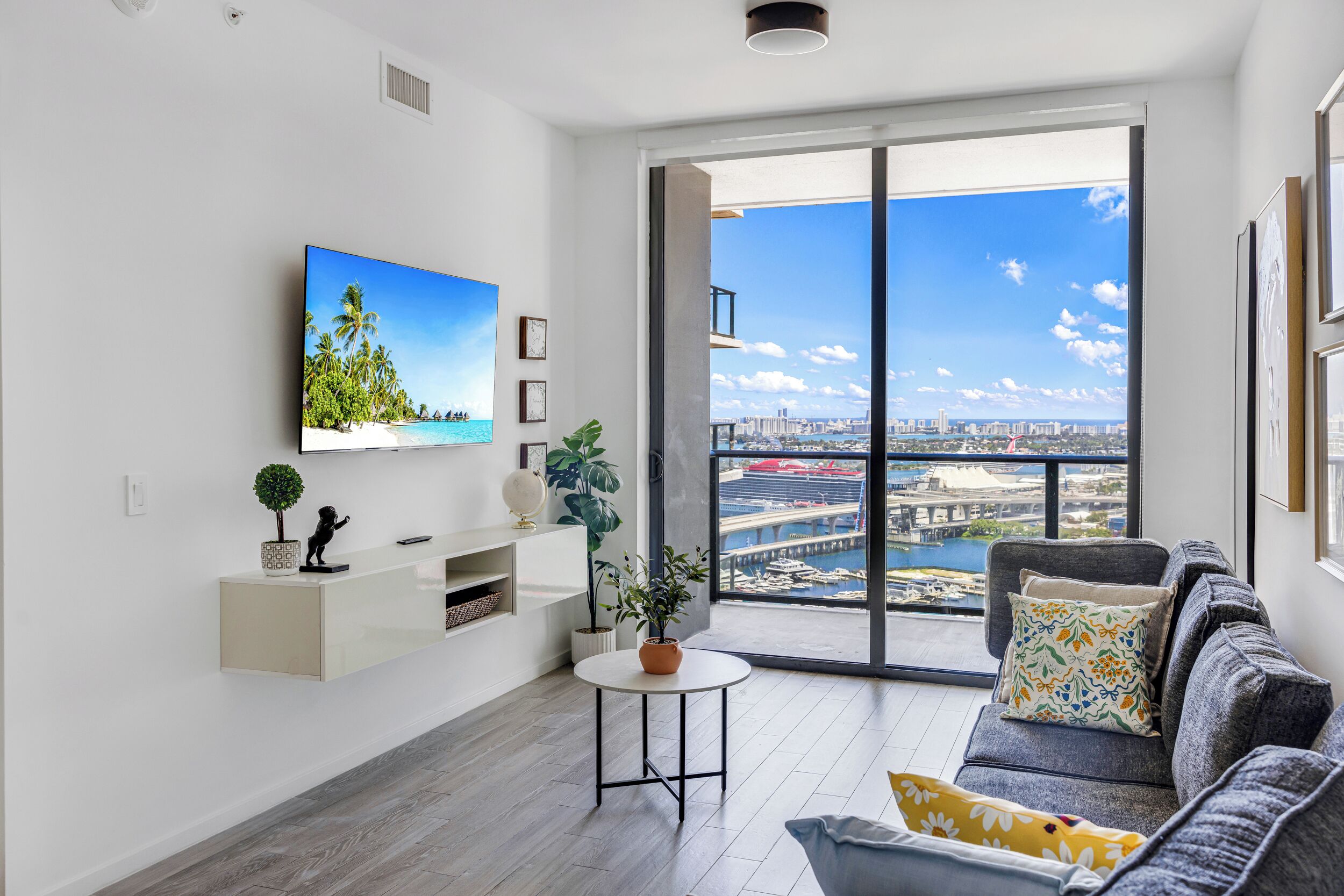 A modern living room with a large window, a flat-screen TV, a sofa, and a small table with a plant.