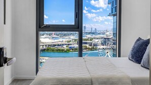 Ein Schlafzimmer mit großem Fenster, einem Bett und Blick auf Stadt und Wasser.