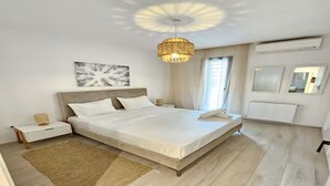 Une chambre à coucher comprenant un lit, des tables de chevet, un luminaire suspendu, une fenêtre avec des rideaux et un radiateur.