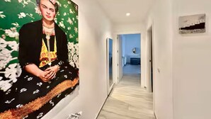 Un couloir orné d’une grande fresque florale sur le mur de gauche, une porte sur le mur de droite, et, au fond, on aperçoit une pièce.