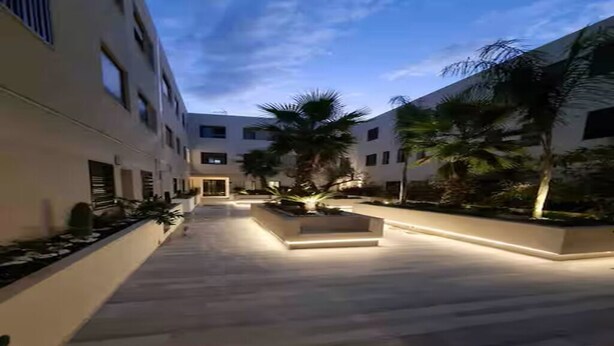 Un bâtiment moderne doté d’une cour intérieure, d’un espace extérieur aménagé pour s’asseoir et de palmiers.