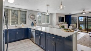 Uma cozinha moderna com armários azul escuro, bancada branca e iluminação pendente.