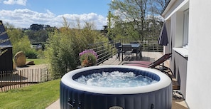 Ein Whirlpool im Freien auf einer Terrasse mit Tisch und Stühlen, umgeben von einem Zaun und viel Grün.