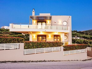 Ein modernes, zweistöckiges Haus mit Balkon, umgeben von angelegten Gärten.