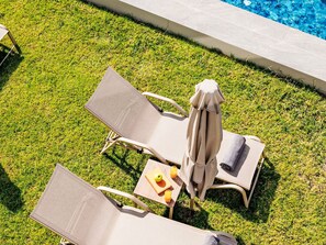 Zona de piscina con dos sillas de descanso, una mesa con un libro, una manzana y dos vasos de jugo de naranja.