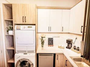 Eine kleine Küche mit Waschmaschine, Kaffeemaschine und einer Tafel mit einer Willkommensbotschaft.