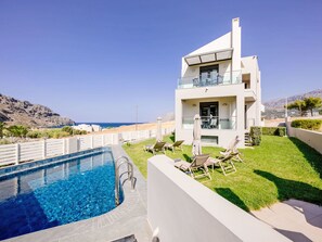 Une maison moderne à deux étages, dotée d’une piscine, d’un espace de détente extérieur et offrant une vue sur la mer.