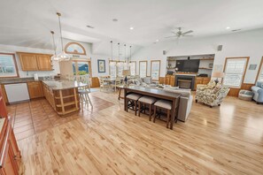 Eine geräumige Küche mit Holzschränken, ein Essbereich mit großem Tisch und ein Wohnzimmer mit Sofa und Fernseher.