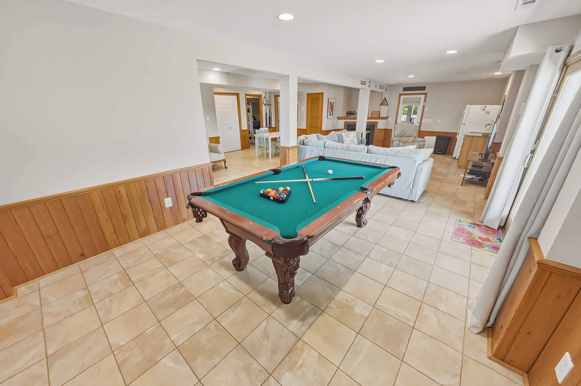 A pool table in a room with a tiled floor, a sofa, and a door leading to another room.