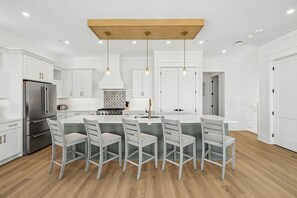 A modern kitchen with white cabinetry, a central island with bar stools, and a stainless steel refrigerator.