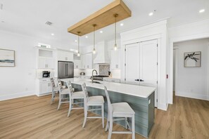 A modern kitchen with white cabinetry, a central island, pendant lighting, and a wooden ceiling beam.