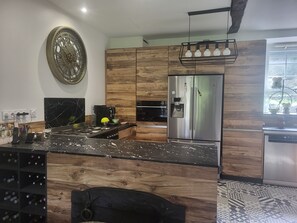 Eine moderne Küche mit Edelstahlkühlschrank, Holzschränken, einer Marmor-Spritzschutzwand und einem Weinkühlschrank.