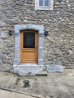 Ein Steinhaus mit Holztür, Steintreppe und einem Fenster darüber.