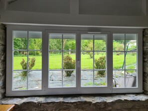 Ein großes Fenster mit steinernen Sockeln, das einen Blick auf einen grünen Garten mit Bäumen und Sträuchern bietet.