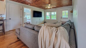 Un salon chaleureux avec un plafond en bois, un canapé gris, un téléviseur et une fenêtre donnant sur un beau paysage.