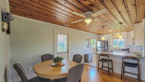 Un coin repas avec une table ronde, des chaises, un ventilateur de plafond et une cuisine en arrière-plan.