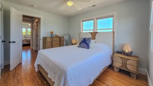 Une chambre à coucher avec un lit, une commode en bois, des lampes de chevet, un ventilateur de plafond et une fenêtre.