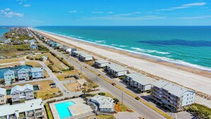 Ein Küstenhotel mit langer Strandpromenade, einem Schwimmbad und einer parallel zum Strand verlaufenden Straße.