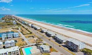 A coastal hotel with a long beachfront, a swimming pool, and a road running parallel to the beach. - Queen's Grant E-216 - NEW - Open Summer Weeks! (Topsail Beach)