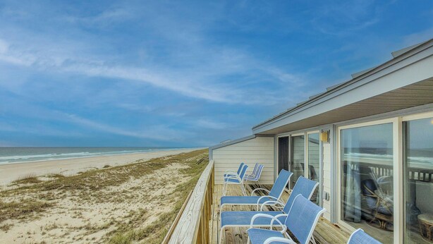 Ein Strandhaus mit einer Terrasse, blauen Stühlen und Blick auf den Ozean.