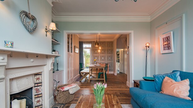 A living room with a fireplace, a blue sofa, and a dining area with a table and chairs. - Whispering Waves, Hythe (Hythe)